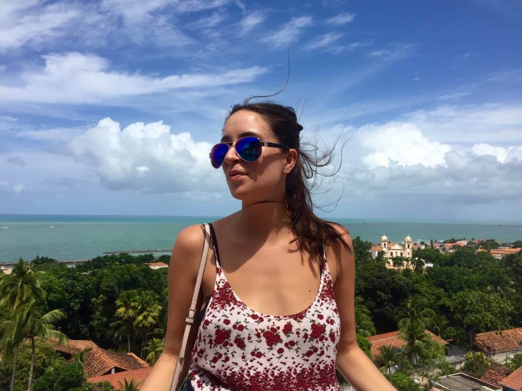 A woman stands on a balcony that overlooks an ocean. 