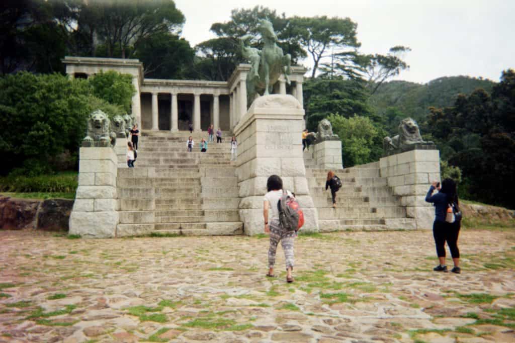 Travelers walking towards stairs that lead up to a statue of a man riding a horse.
